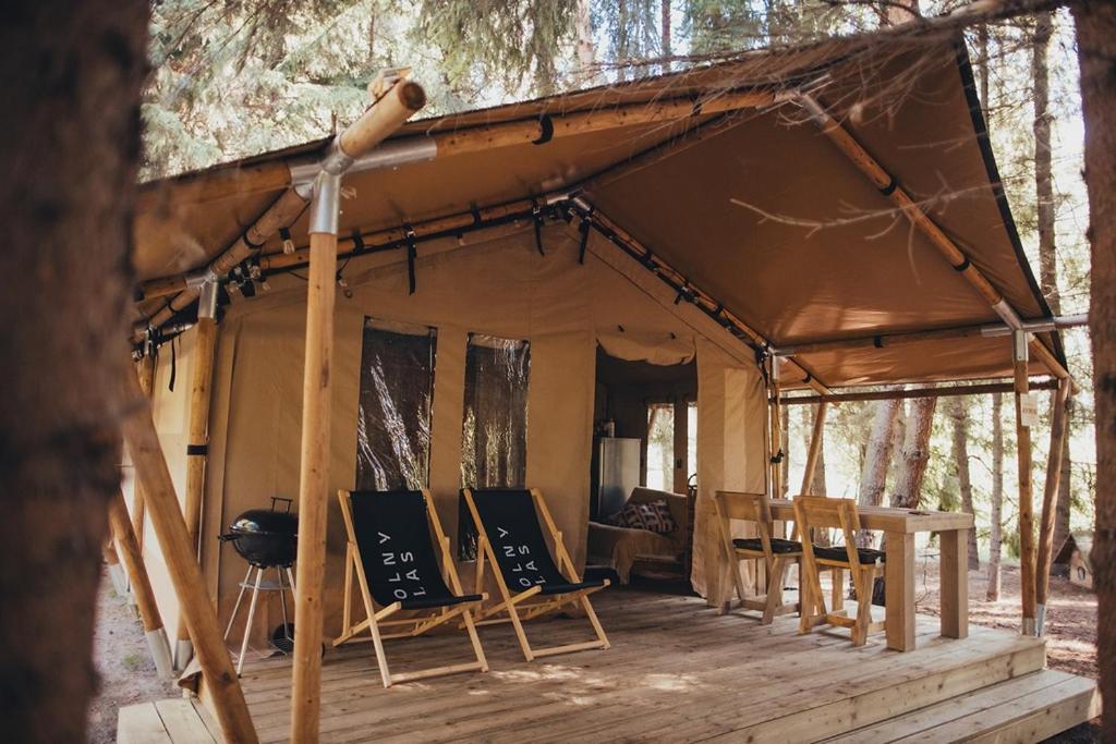 ŁawkiWolny Las Glamping na Mazurach的一个带椅子的帐篷和树林中的烧烤架