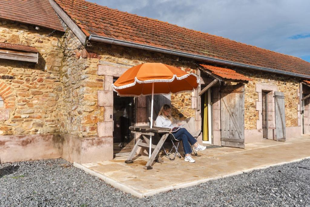 une femme assise sur une chaise sous un parapluie dans l'établissement Gîtes Domaine Bonneblond, à Saint-Désiré