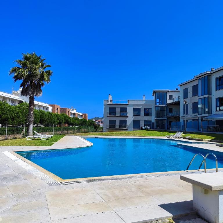a swimming pool with a palm tree and buildings at Casa dos Medros in São Martinho do Porto