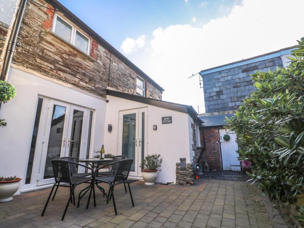 Un patio con una mesa y sillas frente a una casa. en Mews Cottage, en Tintagel