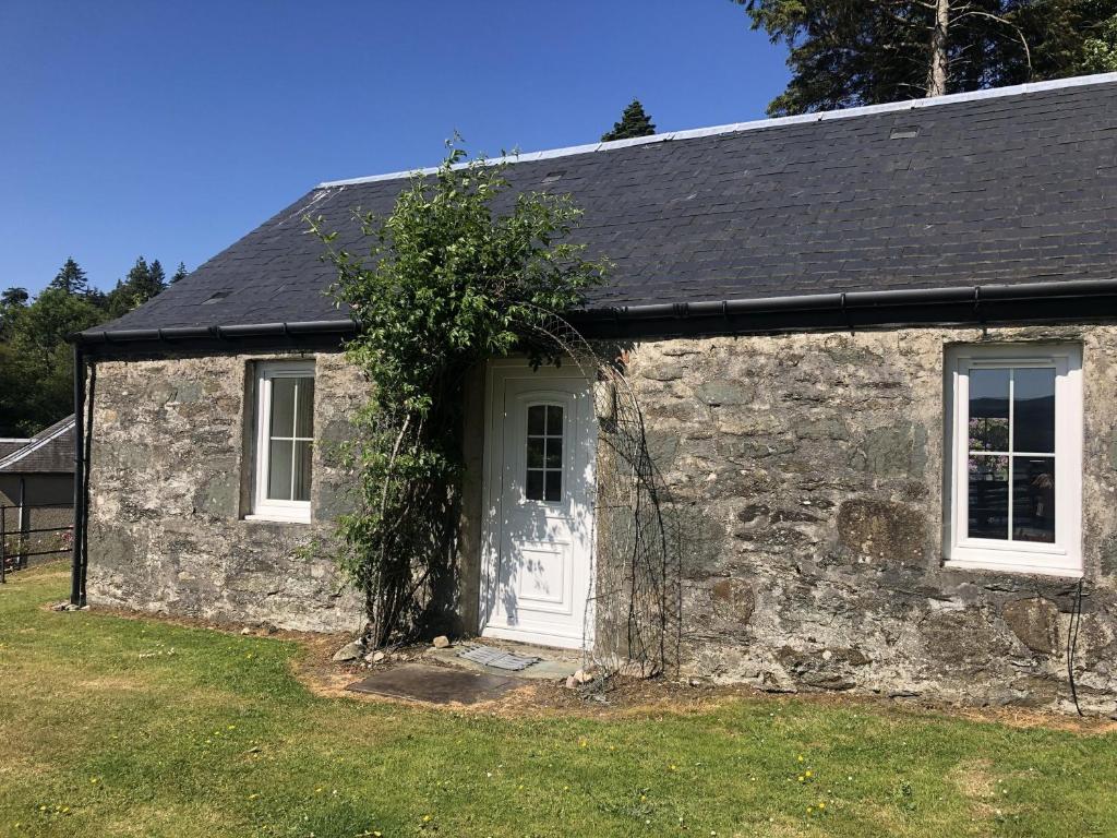 een oud stenen huis met een witte deur en een boom bij Ellary Cottage in Stonefield