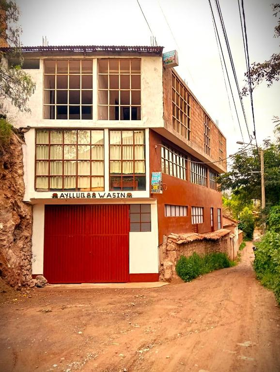 a building with a red door on a dirt road at Hostal Aylluq Wasin Casa de Familia-Guest House, habitación Familiar in Urubamba