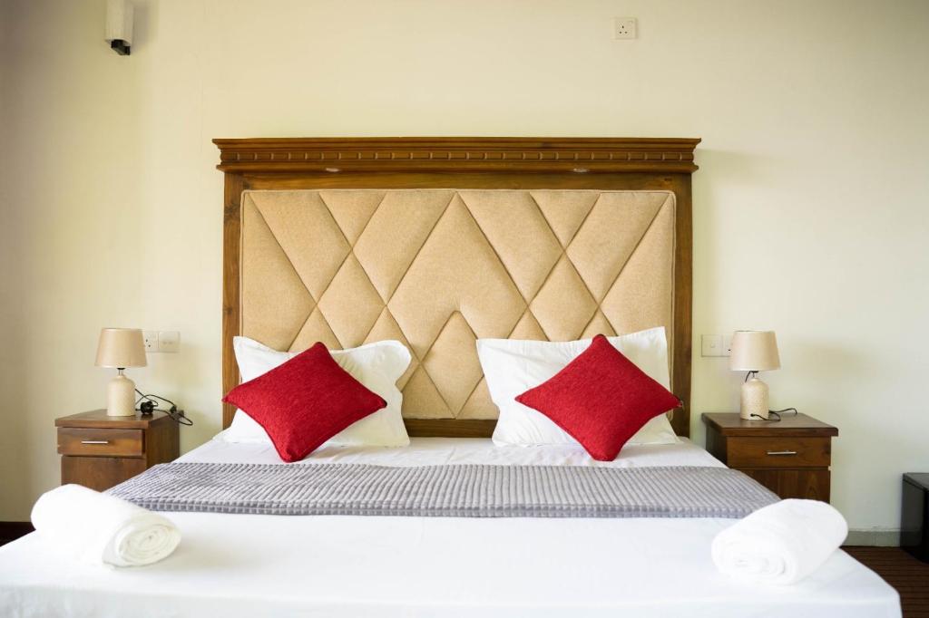 ein Schlafzimmer mit einem großen Bett mit zwei roten Kissen in der Unterkunft Beragala Estate and Resort in Haputale