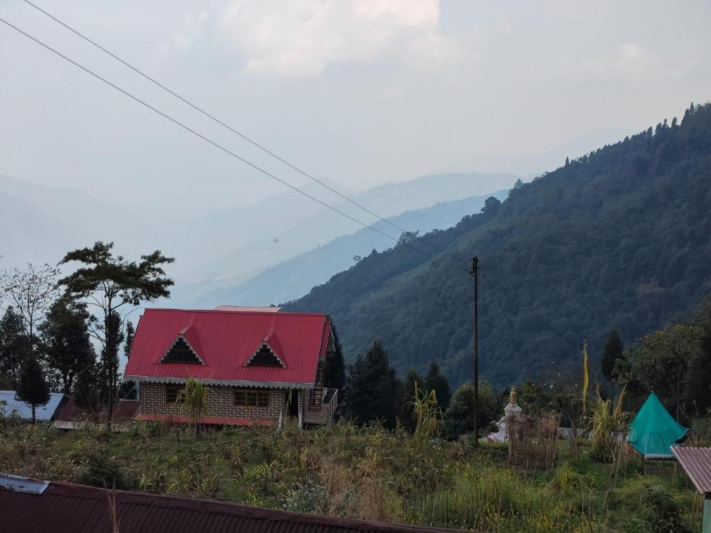 una casa con techo rojo con montañas al fondo en Krishna Cottage Rampuria, en Jālāpahār