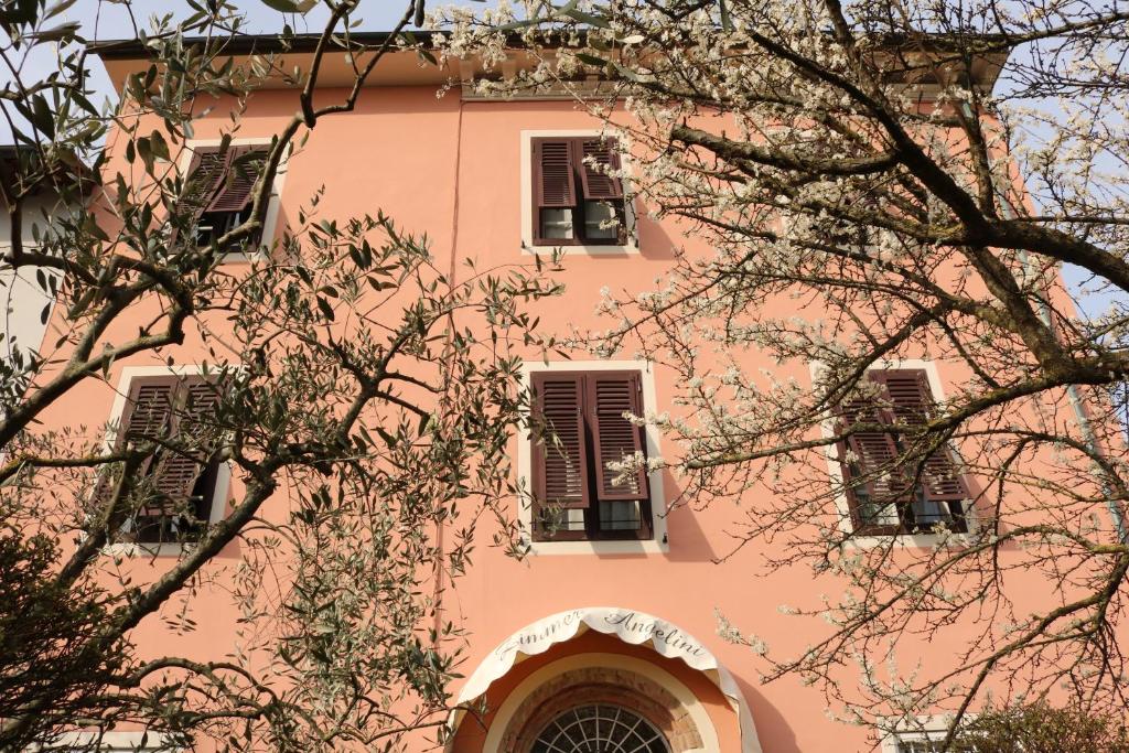 ein rosafarbenes Gebäude mit drei Fenstern und einem Baum in der Unterkunft Angelini in Lucca