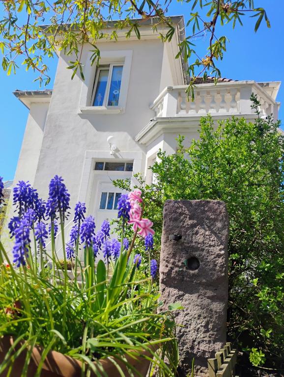 un bâtiment blanc avec des fleurs violettes devant dans l'établissement Gîte Le Marronnier - au calme - parking & terrasse - près de Colmar et Riquewihr - route des vins, à Châtenois