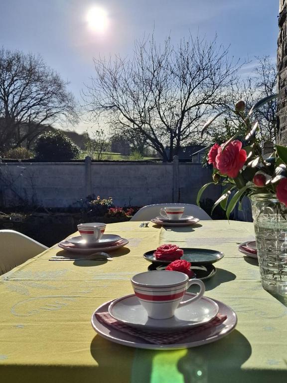 une table avec des tasses, des soucoupes et des fleurs dans l'établissement Gite Mont Saint Michel Chez Pépé Lucien, à La Gohannière