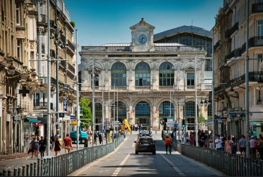 une rue de la ville avec un bâtiment doté d'une tour de l'horloge dans l'établissement SWEET PLAN Appartement 4pers d'exception rue Faidherbe Face Gare Lille Flandres, à Lille