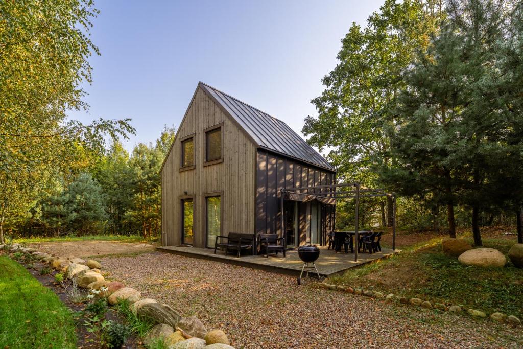 a barn style house with a patio and a grill at Leno Tu - Domki przy jeziorze z sauną i banią in Ciemno