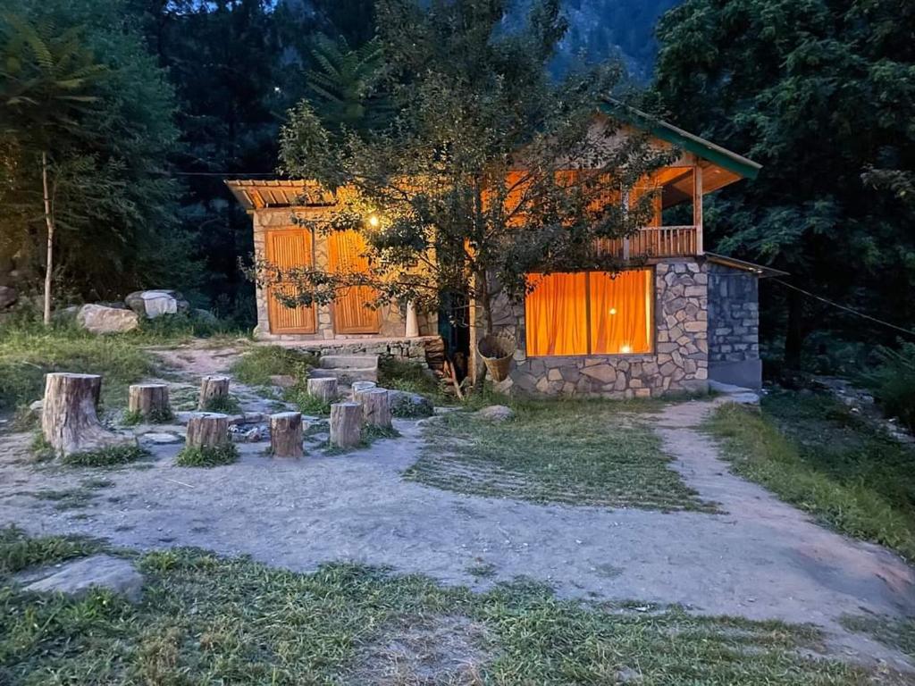 a stone house with a balcony and a tree at Moksha By The River,Jibhi in Jibhi