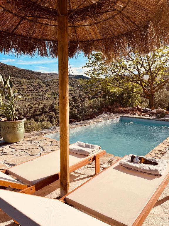 a resort pool with two lounge chairs and an umbrella at Cortijo La Pedriza in Iznájar
