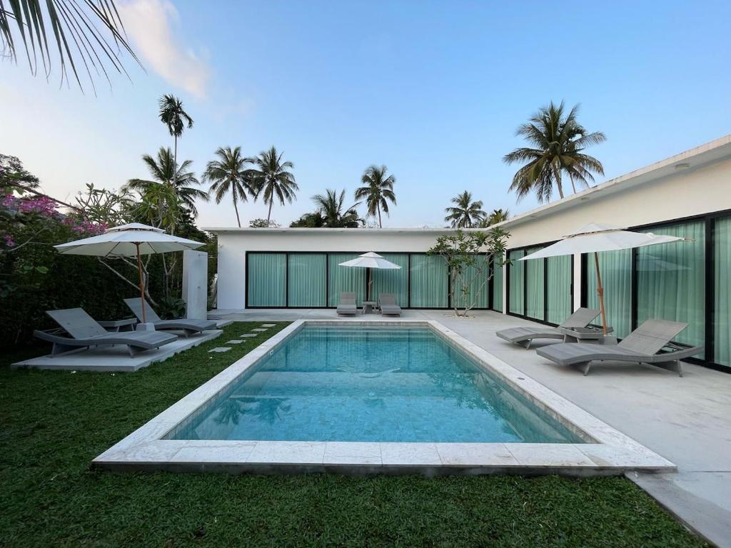 a swimming pool with chairs and umbrellas next to a house at LAILA Villas in Koh Samui 