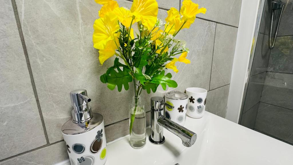 un jarrón de flores amarillas sentado en el lavabo del baño en Cosy and Comfy Deluxe Entire Apartment, en Londres