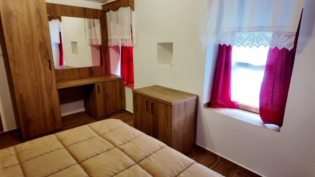 a bedroom with a bed and two windows with red curtains at Suite of Bazaar in Gjirokastër