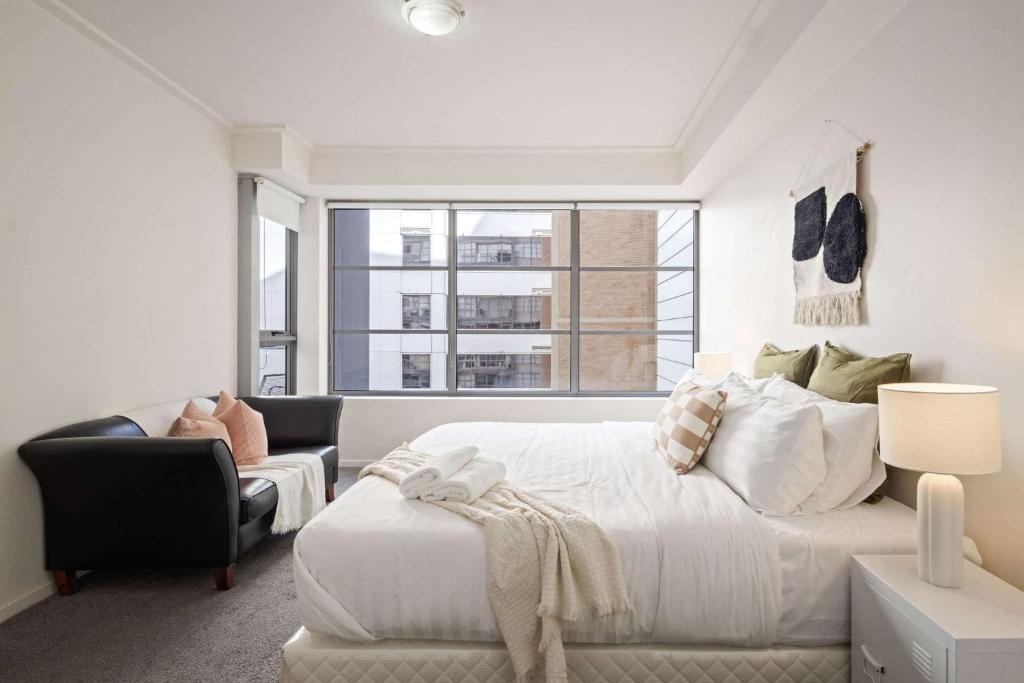Un dormitorio blanco con una cama grande y un sofá. en Cozy 2BR Apartment Steps from Darling Harbour, en Sídney