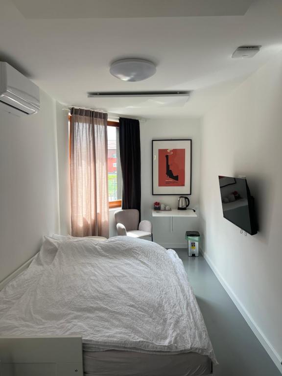 a white bedroom with a bed and a chair at Oasis Airport Apartments and Rooms in Velika Gorica