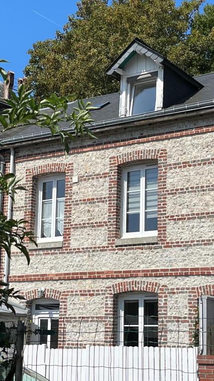 une maison en briques avec deux fenêtres et une clôture blanche dans l'établissement Les Cailloux Verts, à Étretat