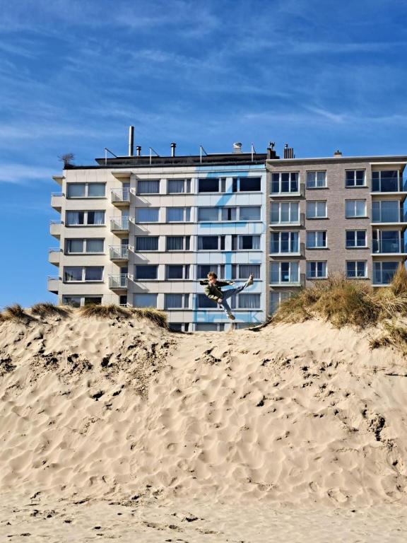 a person jumping off a beach in front of a building at Oostduinkerke Estacade ZEEDIJK in Oostduinkerke