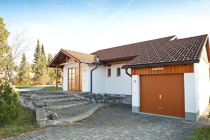 a small white house with brown doors and a driveway at Ferienhaus im Feriendorf Reichenbach B19 in Nesselwang