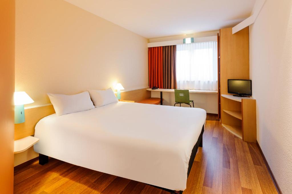 una camera d'albergo con un grande letto bianco e una TV di ibis Berlin Dreilinden a Kleinmachnow
