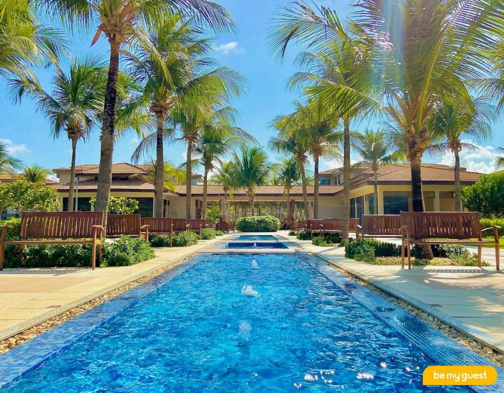 a swimming pool with palm trees in front of a house at Mandara Lanai Resort - Porto das Dunas in Aquiraz