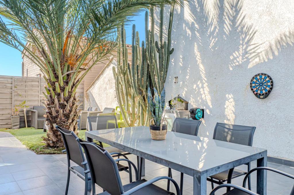 une table et des chaises sur une terrasse avec des palmiers dans l'établissement La Maison du Canal - Face à l'Etang - Climatisation - 6 personnes - 5 min de la mer, à Palavas-les-Flots