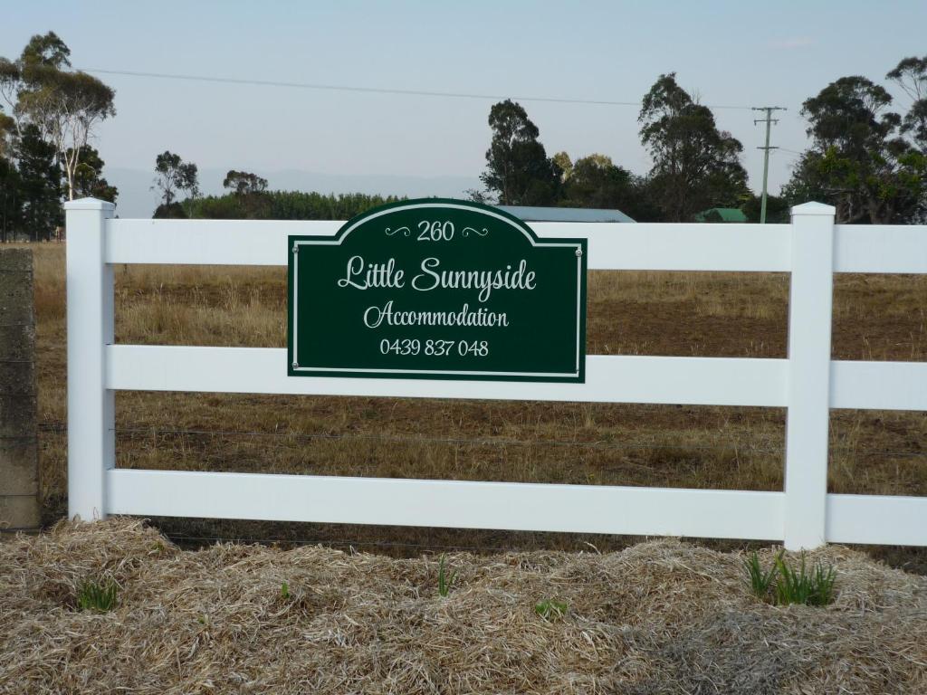 a white fence with a green sign on it at Little Sunnyside Accommodation in Hagley