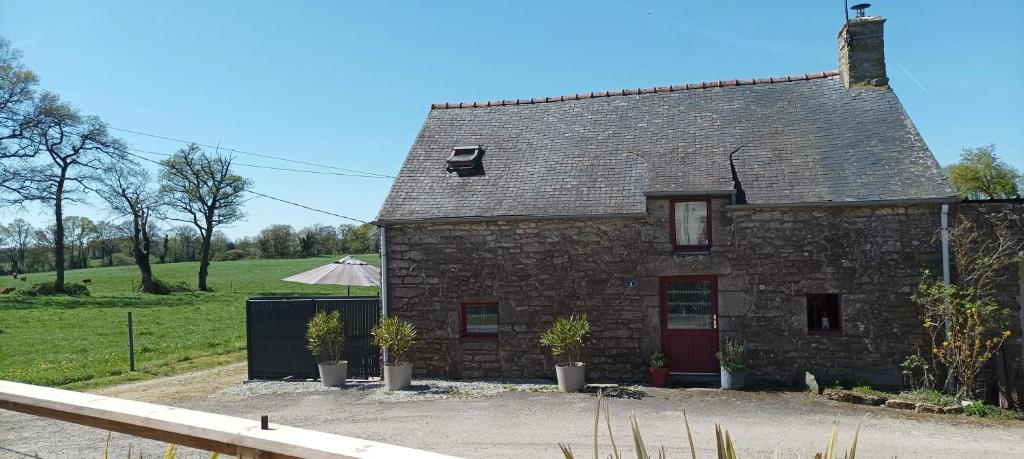 une maison en pierre avec une porte rouge et un champ dans l'établissement Maison confortable à Questembert avec jardin, à Questembert