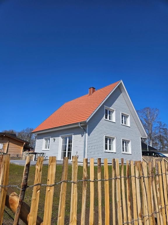 a white house with a red roof behind a fence at Ferienhaus am See mit Sauna in Rheinsberg