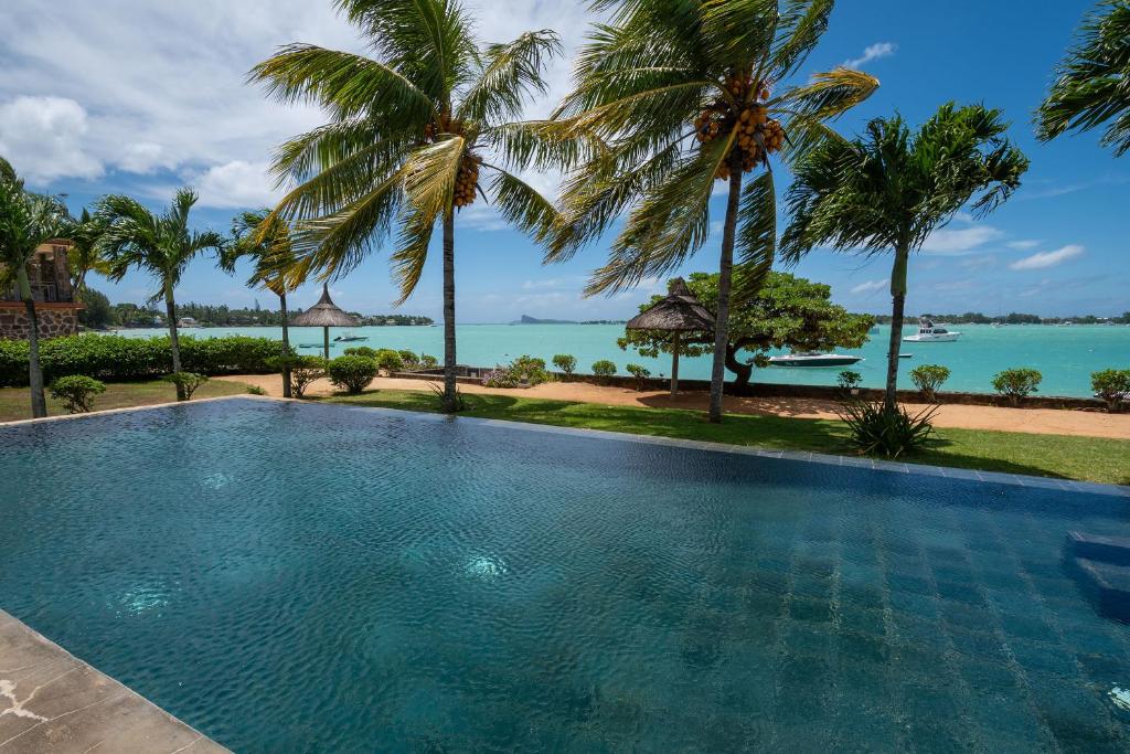 a swimming pool with palm trees and the ocean at 4- Bedroom Beachfront Villa in Grand Baie