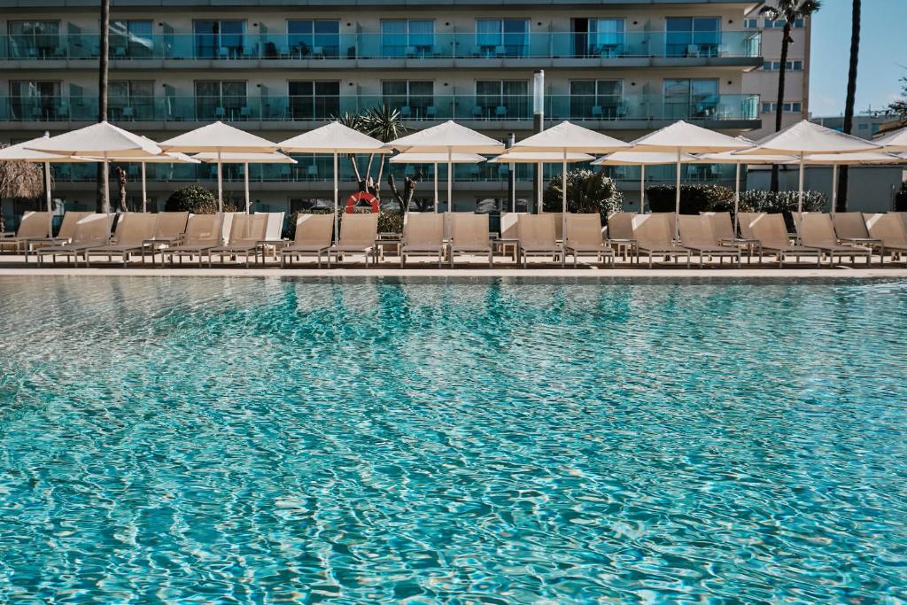 a pool with chairs and umbrellas in front of a hotel at Helios Mallorca Hotel & Apartments in Can Pastilla