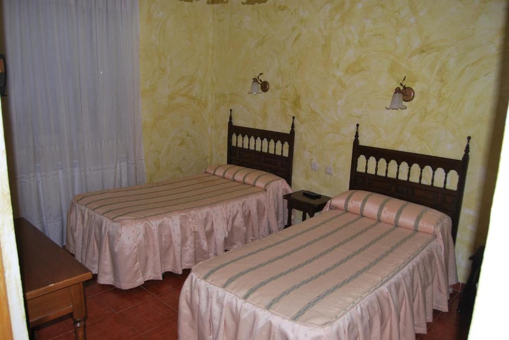 two beds in a room with yellow wallpaper at Hostal Bellas in Ávila