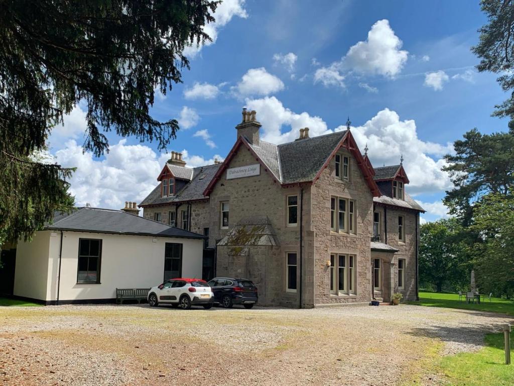 ein großes Haus mit zwei davor geparkten Autos in der Unterkunft Dalrachney Lodge Hotel in Carrbridge
