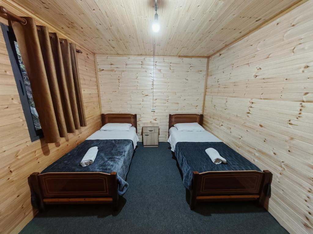two beds in a room with wooden walls at Riverside Komani Lake in Koman