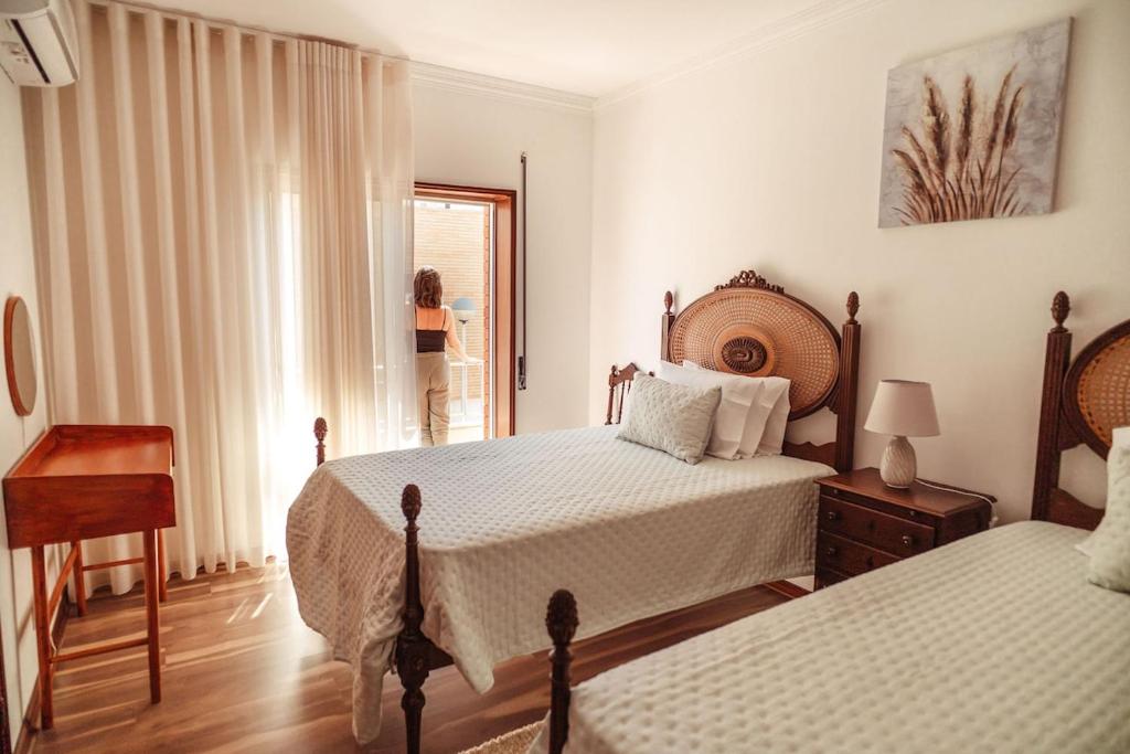 a bedroom with two beds and a woman standing in a window at Moledo's Sea House in Moledo
