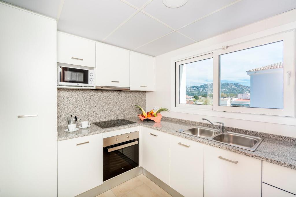 a kitchen with white cabinets and a sink and a window at Apartaments Condado by Marsol in Lloret de Mar