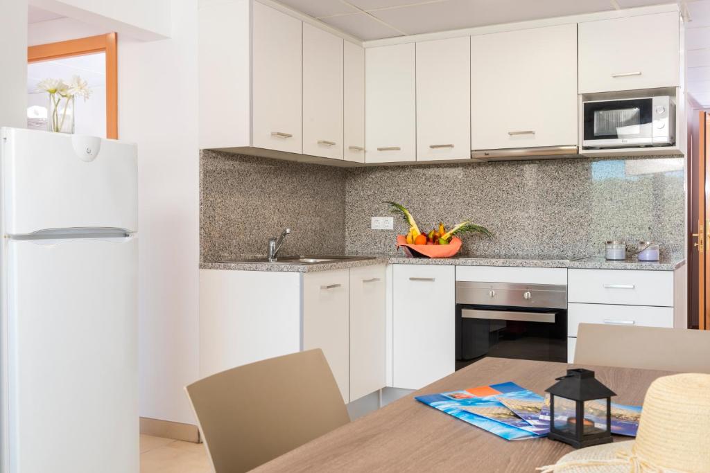 a kitchen with white cabinets and a wooden table at Apartaments Condado by Marsol in Lloret de Mar