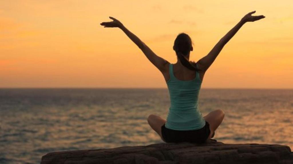 a woman sitting on a rock by the ocean with her arms outstretched at 701 Mariners Club in Key Largo