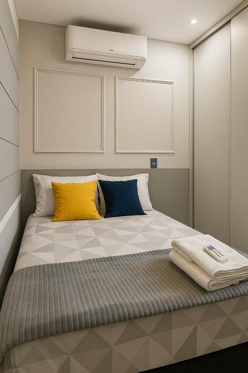 a bed with yellow and blue pillows in a room at Apartamento de Luxo com Suíte, Academia, Piscina e Mercado in Cuiabá