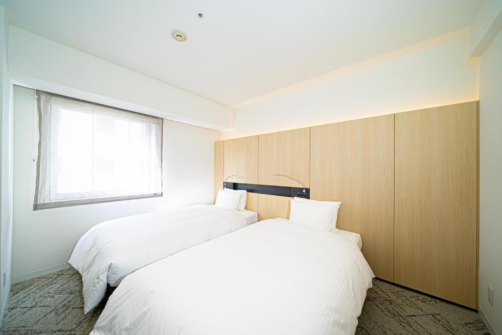 two beds in a bedroom with a window at Hotel Sunroute Tokushima in Tokushima