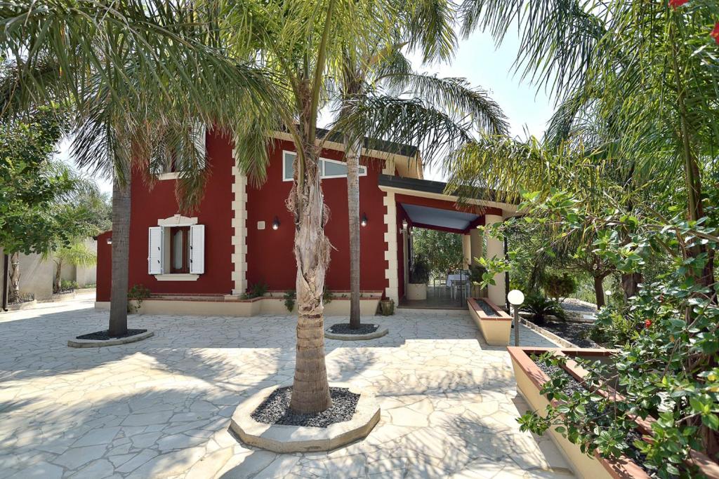 un palmier devant une maison rouge dans l'établissement Villa del Colle con piscina privata, à Ispica
