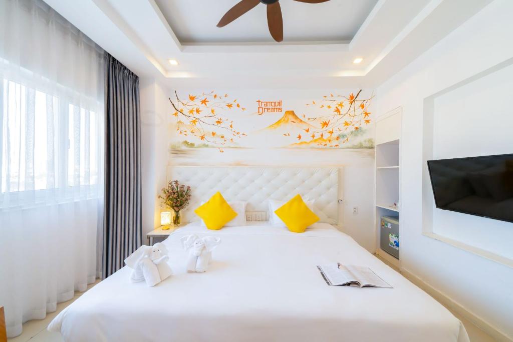 A white bedroom with yellow accents, a large bed, television and curtained window.