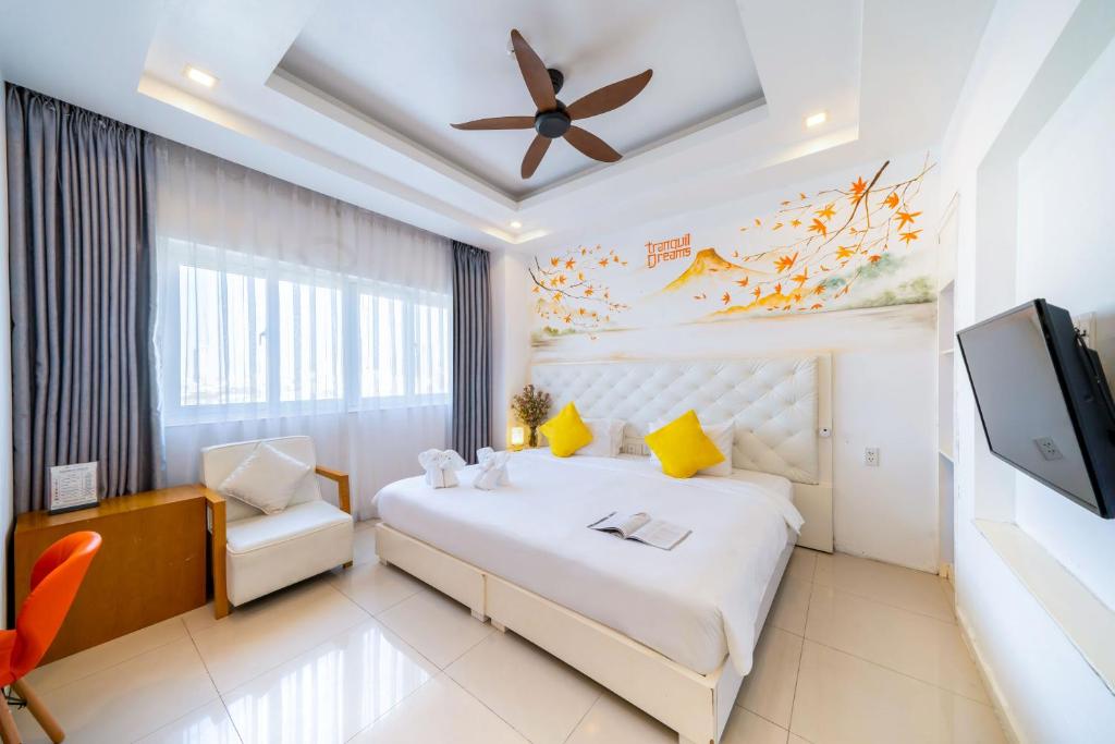 A bright bedroom with a large bed, armchair, desk, television and curtained window.