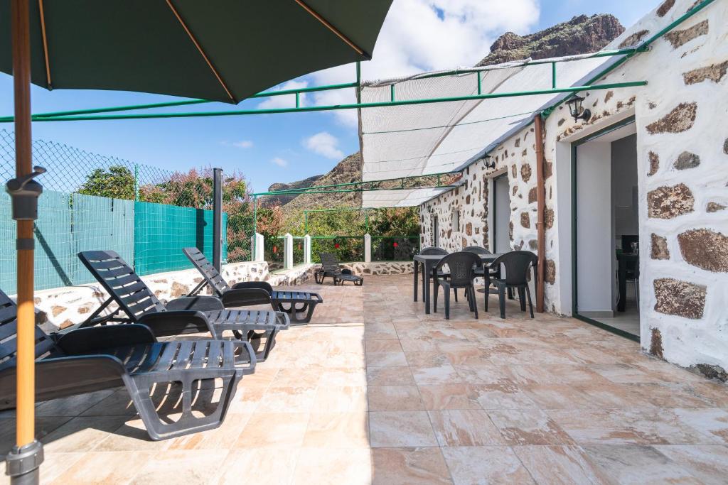 a patio with chairs and tables and an umbrella at Home2Book Mountain Serenity House Agaete, Terrace in Agaete