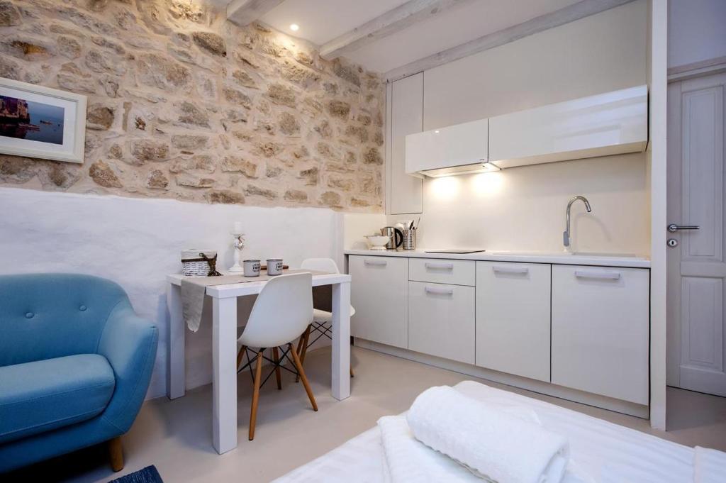 a kitchen with white cabinets and a table and a blue chair at Luna Rooms and Studios Rovinj in Rovinj