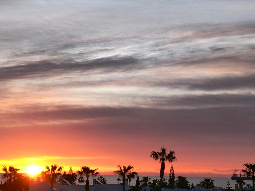 a sunset over the beach with palm trees at vera playa atico balcón al mediterráneo in Vera