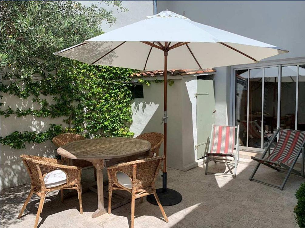 ein Tisch und Stühle mit einem Sonnenschirm auf einer Terrasse in der Unterkunft ORIANE maison de charme proche Plage in Sainte-Marie-de-Ré