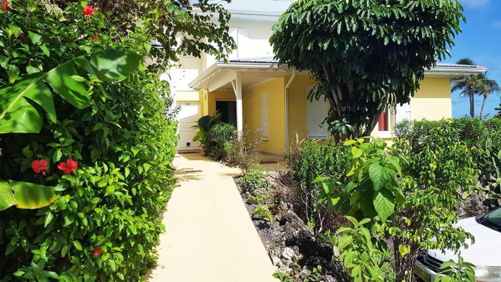 a garden with a yellow house with trees and flowers at La Parenthèse de L'Autre Bord, donnant sur la plage in Le Moule