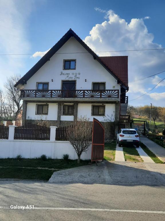 a white house with a car parked in front of it at Pensiunea Maria-Elena in Ponoarele