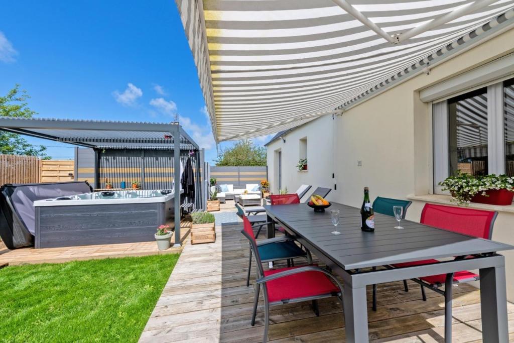 un patio con tavolo, sedie e vasca idromassaggio di Maison spacieuse avec spa , sauna au pays des Abers ,10 min des plages Bretagne a Lannilis